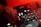 A close-up of a DJ's hand operating a mixing console. The mixer is surrounded by various knobs and buttons, with colored lights illuminating the surface. The scene is bathed in warm red lighting, creating a vibrant and dynamic atmosphere.