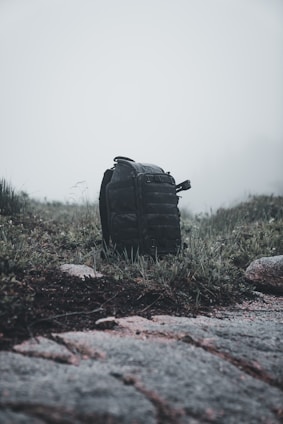 A rugged backpack resting against a weathered wooden fence under a cloudy sky.