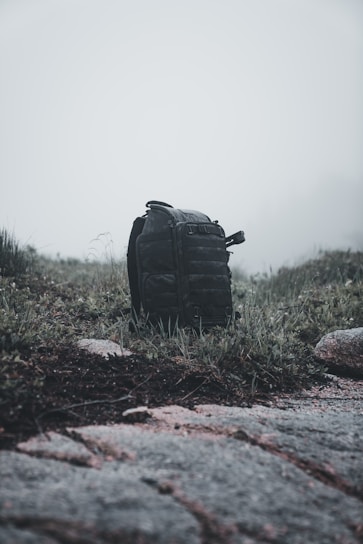 A rugged backpack resting against a weathered wooden fence under a cloudy sky.