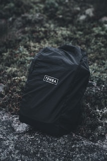 Close-up of a weather-resistant Amsonyns LLC backpack resting on mossy rocks near a forest stream