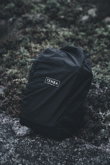 Close-up of a weather-resistant Amsonyns LLC backpack resting on mossy rocks near a forest stream