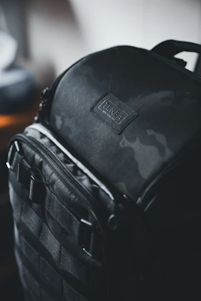 A sleek, matte black travel bag resting on a textured concrete surface with soft natural light highlighting its technical woven texture.