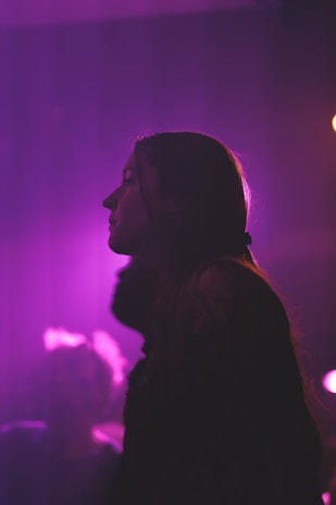 A deep purple-hued still from a music video, showing Saint Amari silhouetted against a smoky backdrop.