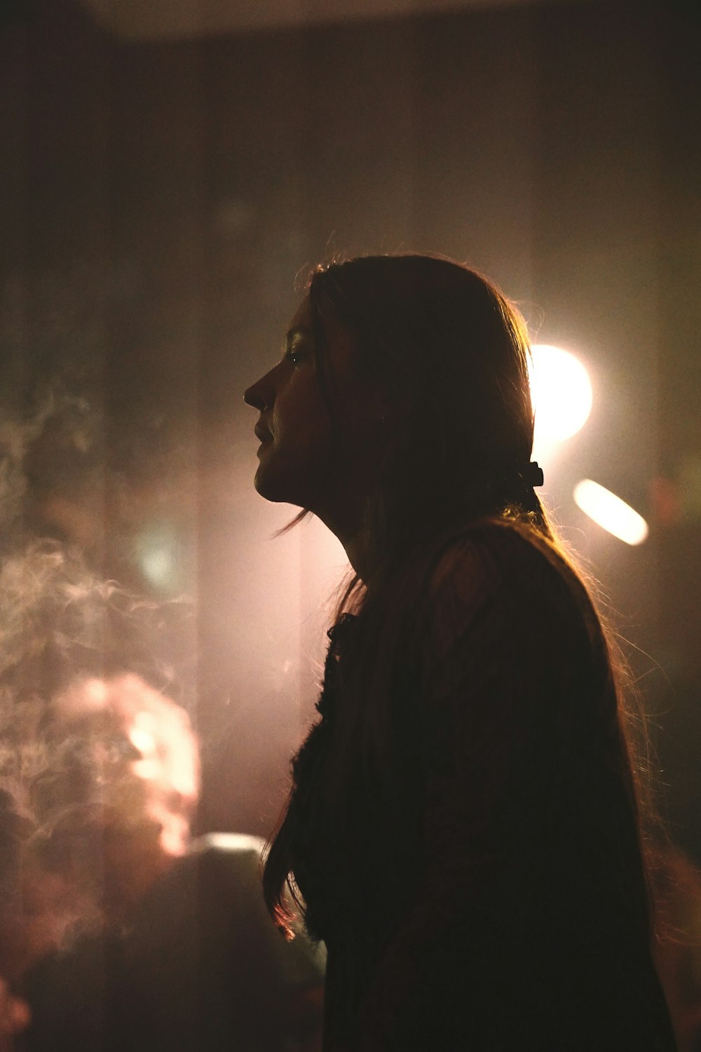 a woman standing in a dark room with smoke coming out of her mouth