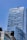 A tall, modern skyscraper with a sleek, glass exterior and a reflective surface under a clear blue sky. The building features the logo of 'The Ritz-Carlton' at the top. In the foreground, part of a traffic light and another building with a contemporary design can be seen.