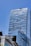 A tall, modern skyscraper with a sleek, glass exterior and a reflective surface under a clear blue sky. The building features the logo of 'The Ritz-Carlton' at the top. In the foreground, part of a traffic light and another building with a contemporary design can be seen.