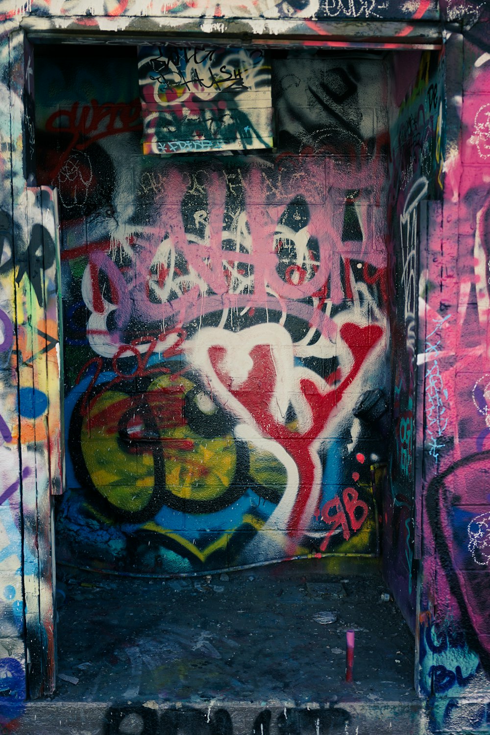 a door covered in lots of graffiti next to a wall