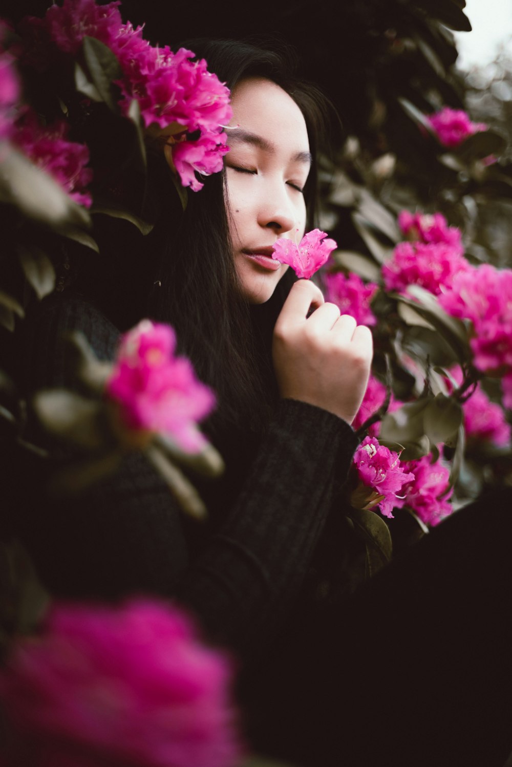 a woman standing in front of a bush of pink flowers