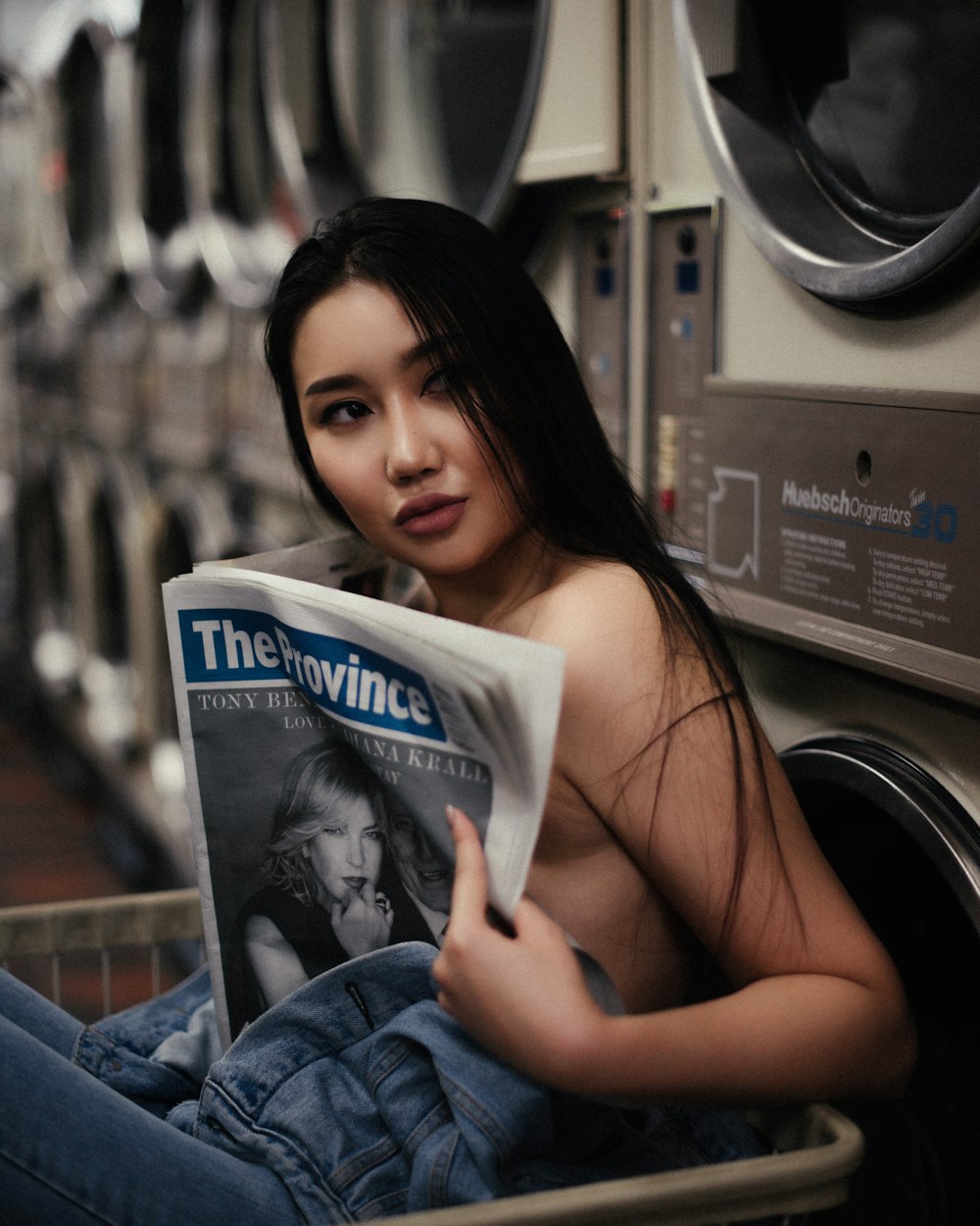 a woman sitting in a laundry machine reading a newspaper