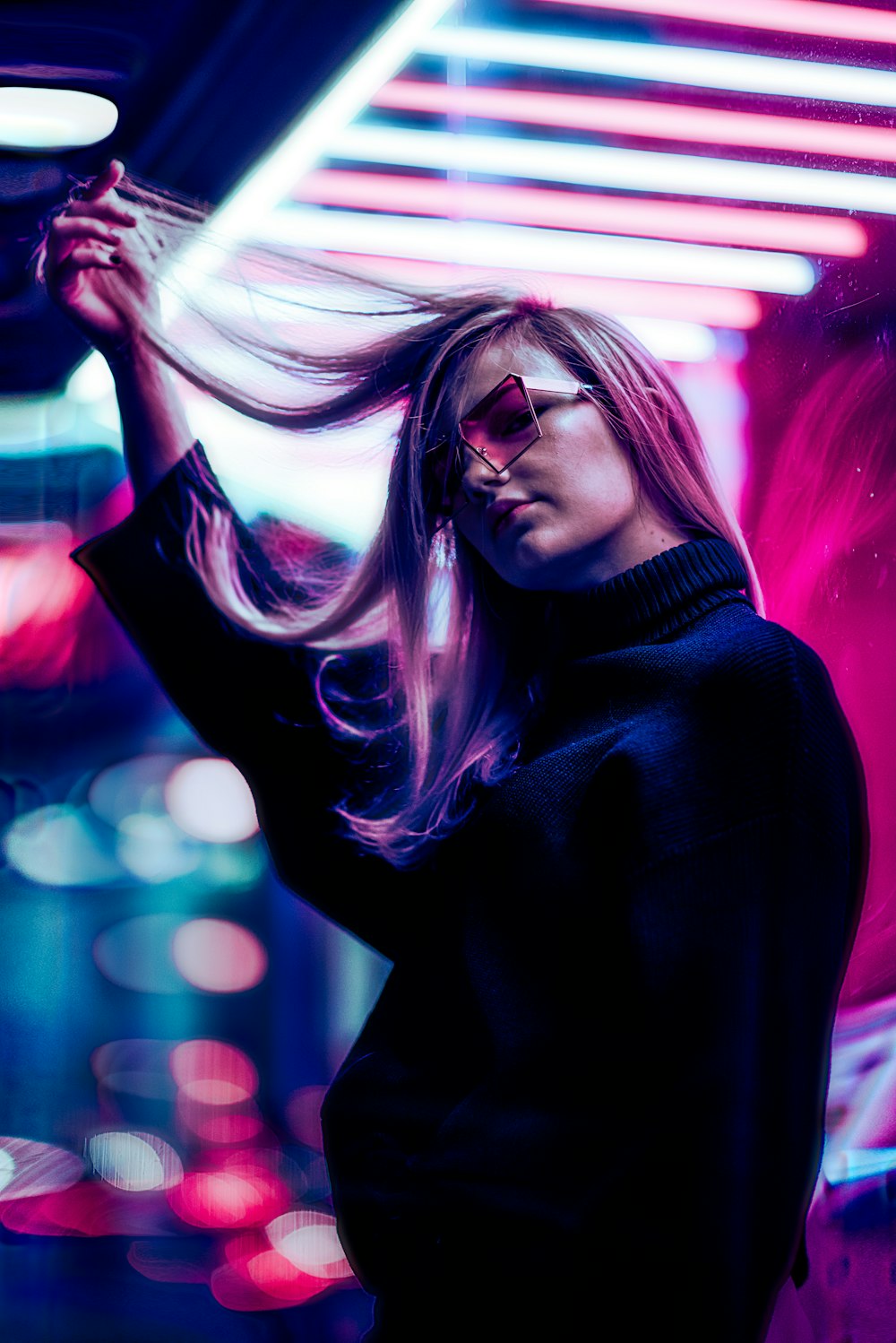 a woman with long hair and sunglasses standing in front of a neon light