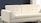 A modern, white, upholstered sofa with a minimalist design and tufted backrest sits in a room with a neutral color scheme. The background features a dark blue wall and contrasting white elements, creating a clean and contemporary aesthetic.