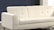 A modern, white, upholstered sofa with a minimalist design and tufted backrest sits in a room with a neutral color scheme. The background features a dark blue wall and contrasting white elements, creating a clean and contemporary aesthetic.