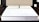 A neatly made bed features a white mattress with two cream-colored pillows. The mattress has a subtle pattern and appears supportive. Situated in a modern bedroom, the bed is flanked by dark wooden nightstands. An elegant, minimalist decor style is evident in the room.