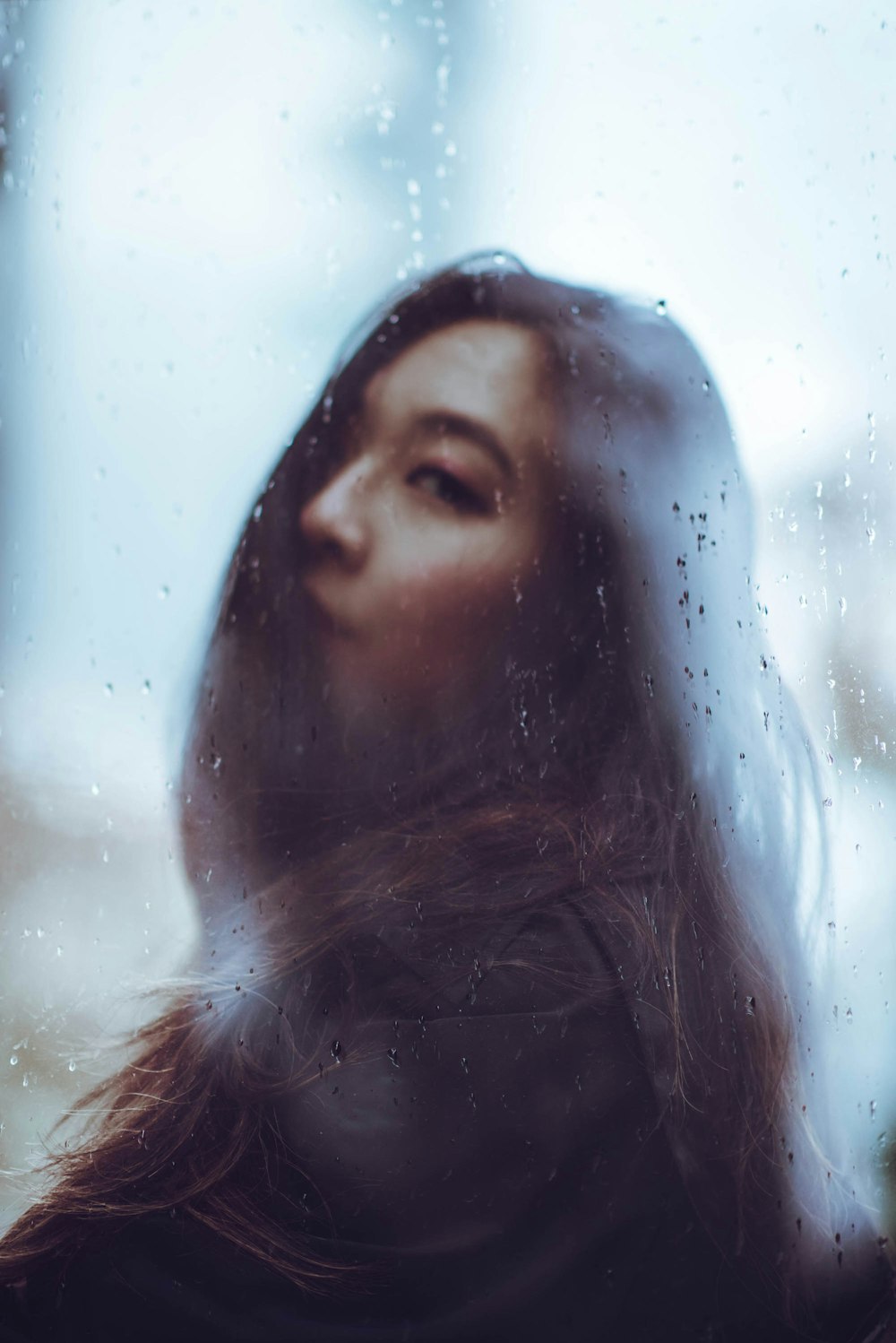 a woman standing in front of a window covered in rain