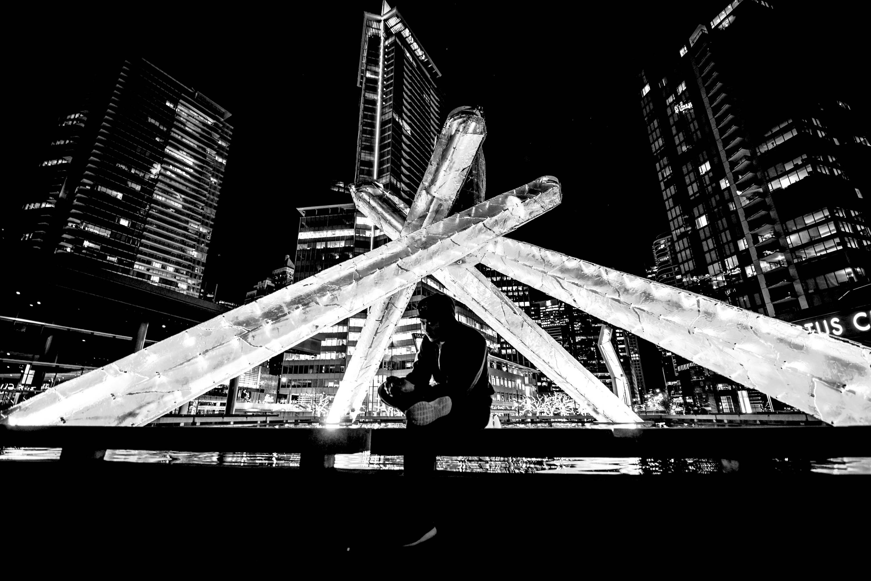 A man sitting on a bench in front of tall buildings photo – Free City ...