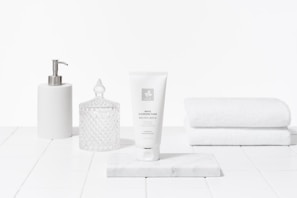 Simple arrangement of skincare tubes in sage green and white tones on clean off-white surface.