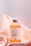 A bottle of vitamin C whitening product is positioned on a peach-colored, silky fabric backdrop. The label on the bottle indicates it contains stem cell ingredients for skin rejuvenation.