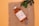 A bottle labeled 'Stem Cell Vitamin C Whitening' is placed on a piece of burlap fabric. Beside it lies a syringe, and some green leaves are placed above the bottle, creating a natural and organic feel. The background is a soft peach color.