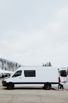 A white minibus parked outside Kiruna airport with snow-covered pine trees in the background.
