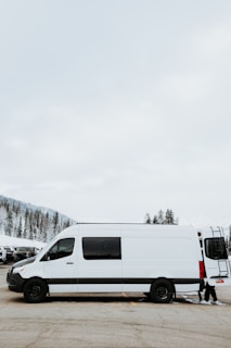 A white minibus parked outside Kiruna airport with snow-covered pine trees in the background.