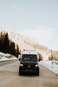 Luxury taxi van parked outside a snowy alpine airport terminal with mountains in the background.