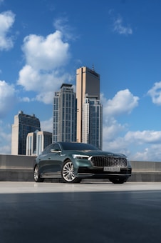 A sleek, modern car is parked on a rooftop with a backdrop of tall skyscrapers under a bright blue sky. The clouds are fluffy and create a vibrant atmosphere. The car's design is elegant and shiny, reflecting the sunlight.