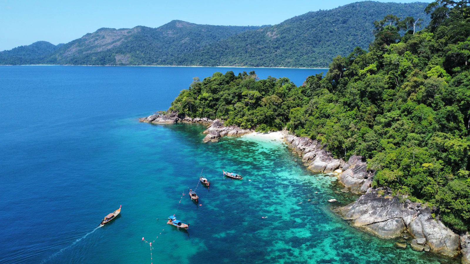 Boats anchored over a coral reef off a jungle island in the Andaman Sea, Thailand