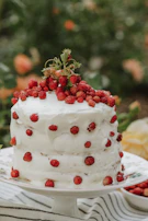 A beautifully frosted cake topped with fresh berries and edible flowers on a rustic cake stand.