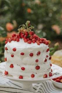 A beautifully frosted cake topped with fresh berries and edible flowers on a rustic cake stand.