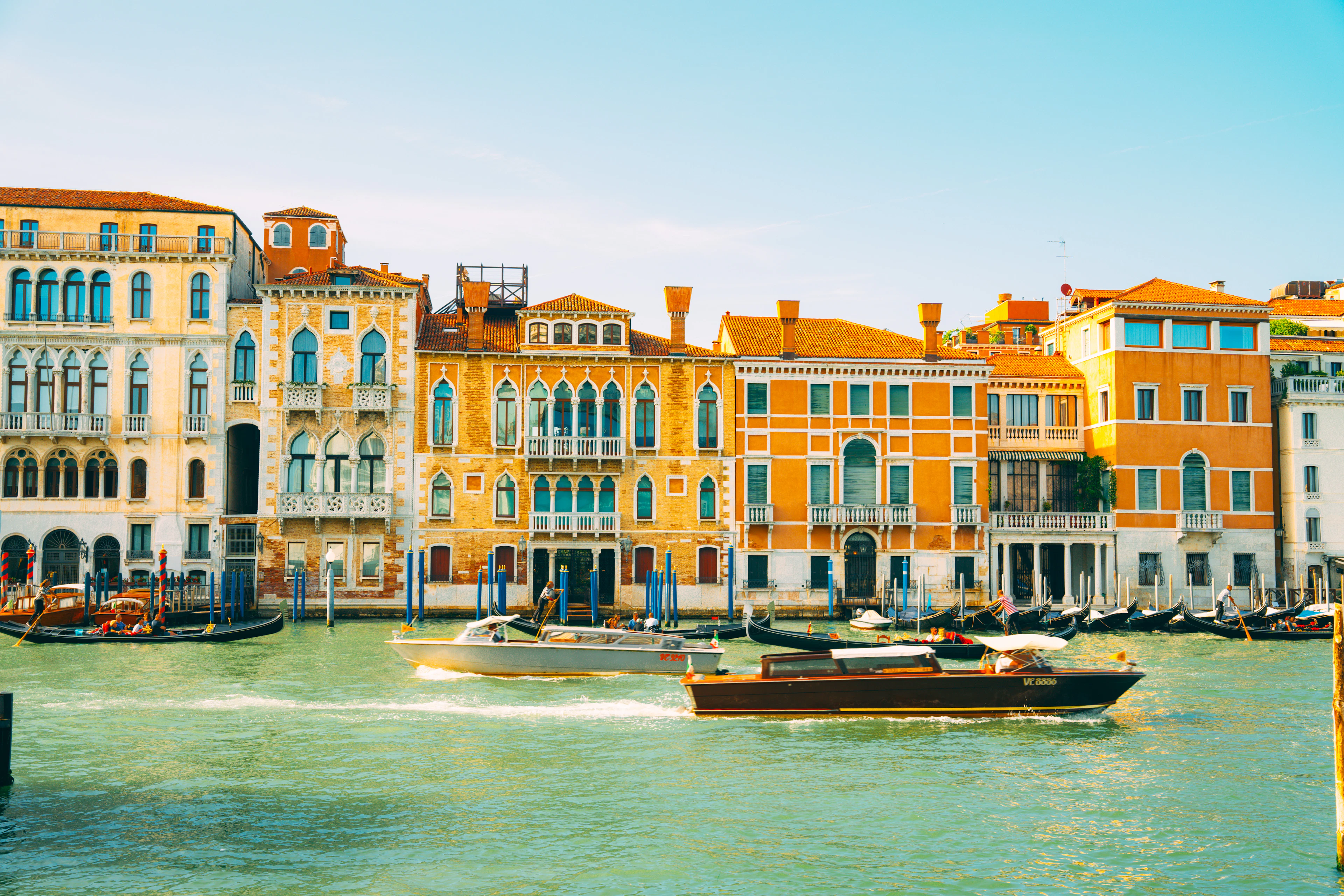 Vaporetto boats cross the Grand Canal in front of a row of ochre and terracotta palazzos.