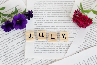 a scrabble of scrabble blocks spelling the word july next to flowers