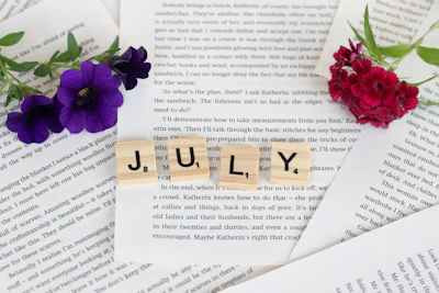 a scrabble of scrabble blocks spelling the word july next to flowers