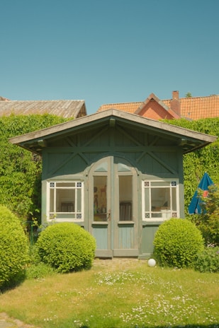 A sturdy steel-frame garden shed with wood-like metal panels under a bright blue sky.