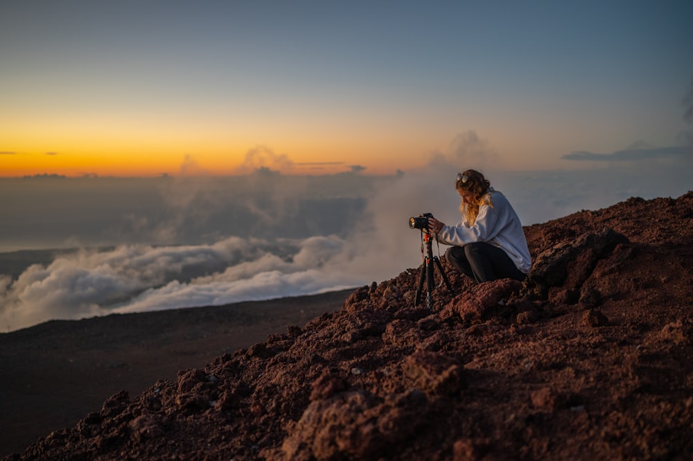 a woman sitting on top of a mountain with a camera