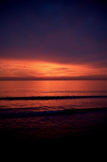 the sun is setting over the ocean on a cloudy day