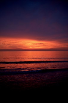 the sun is setting over the ocean on a cloudy day