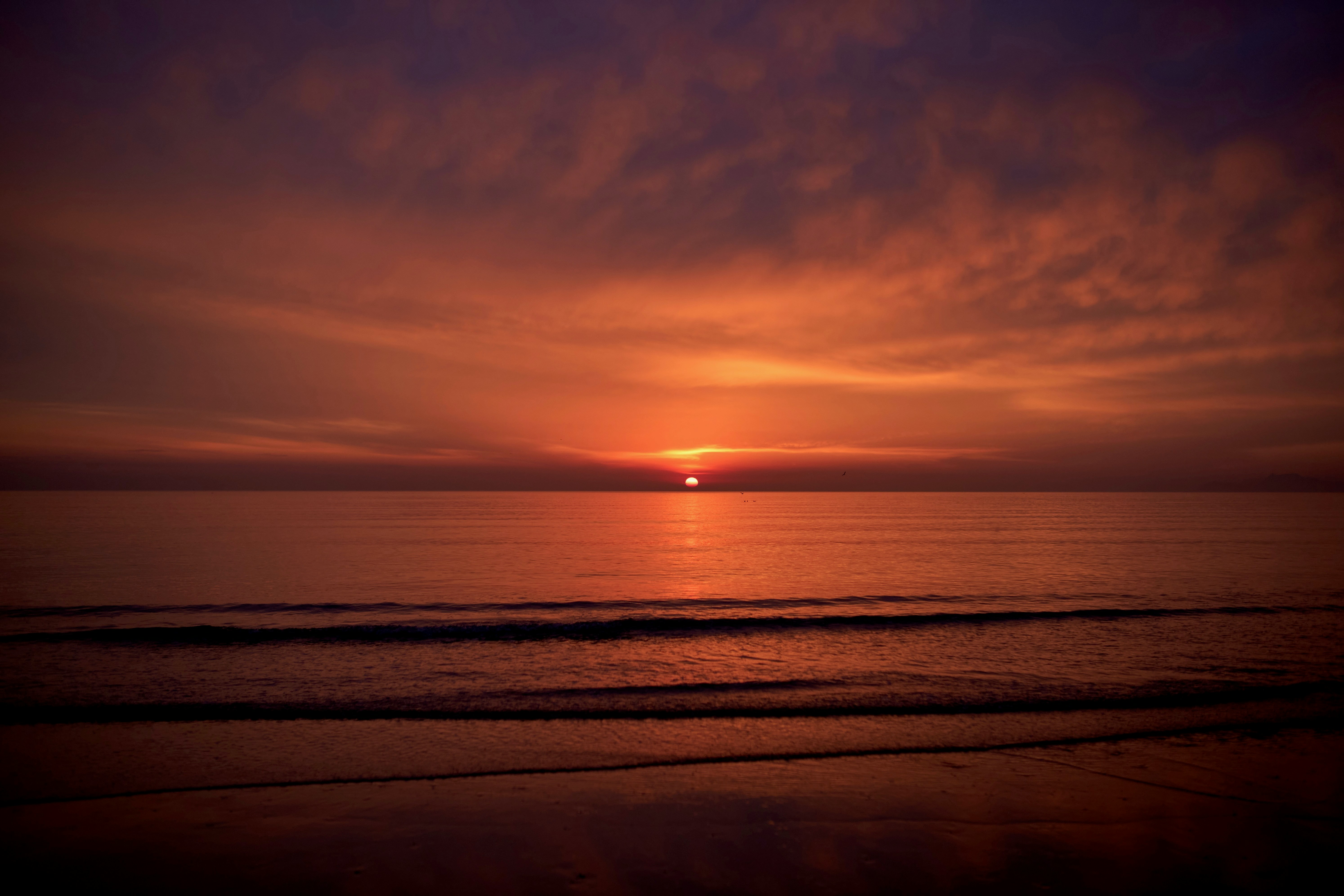 the sun is setting over the ocean on a cloudy day