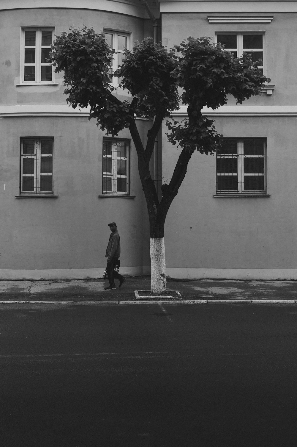 a black and white photo of a man walking past a tree