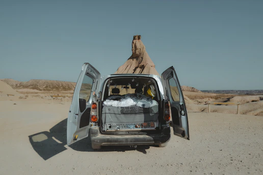 A rugged van parked at sunset in a desert landscape with a lone male traveler preparing gear.