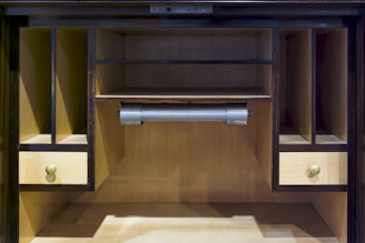 A wooden desk with open shelves and drawers. The interior is a light wood color, while the exterior has a dark finish. Two small drawers with round knobs are positioned on either side. A roll holder is located in the center.