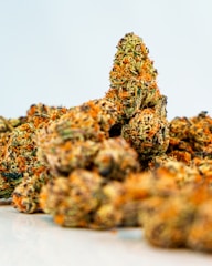 A close-up view of several cannabis buds featuring a mix of green and orange hues. The texture appears dense and covered with trichomes, suggesting a high level of THC.