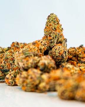 A close-up view of several cannabis buds featuring a mix of green and orange hues. The texture appears dense and covered with trichomes, suggesting a high level of THC.