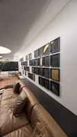 A sleek aluminium metal poster featuring a vibrant abstract design hanging above a modern black leather sofa in a dimly lit living room.
