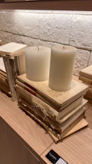 A stack of elegant books bound in black leather with gold embossed titles, resting on a wooden table with a lit candle.