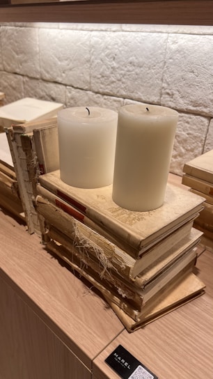 A serene stack of spiritual books beside a softly glowing candle on a wooden table.