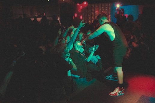 A lively concert scene with a performer engaging with the audience. The crowd is reaching out enthusiastically towards the singer, who is holding a microphone and leaning into the audience. The atmosphere is full of energy and connection, with dim lighting and colorful spotlights creating a dramatic effect.