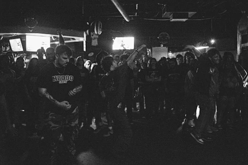 Grainy black-and-white shot of an immersive listening party with engaged audience in a stark concrete space.
