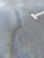 A rough asphalt surface with an iridescent oil spill reflecting a spectrum of colors. A large, white arrow indicating direction is partially visible on the pavement.