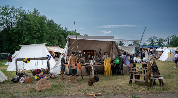 Visitors touching and trying out old crafts at a colorful medieval market scene.