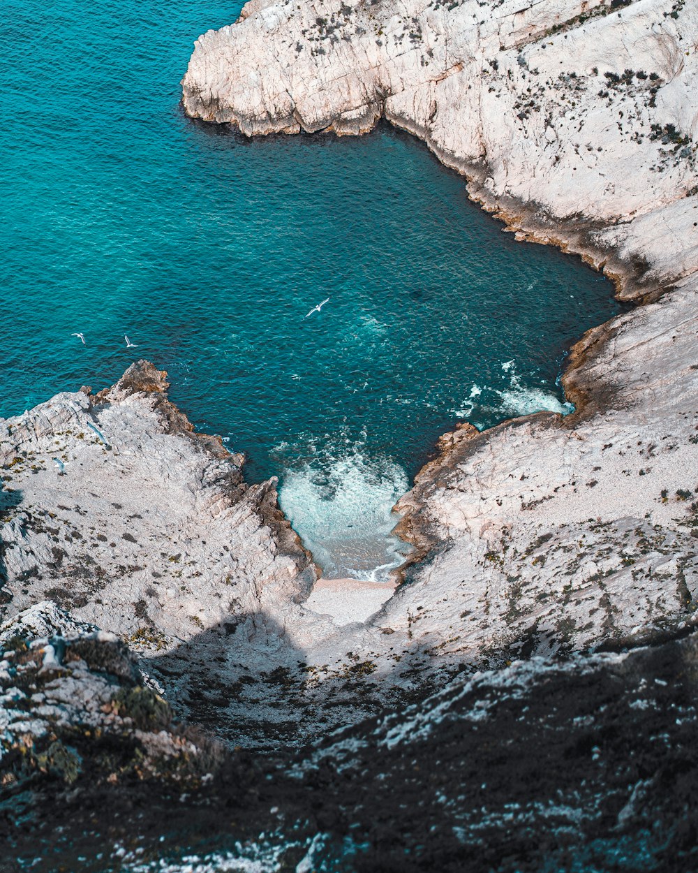 uma vista aérea de um corpo de água perto de um penhasco rochoso